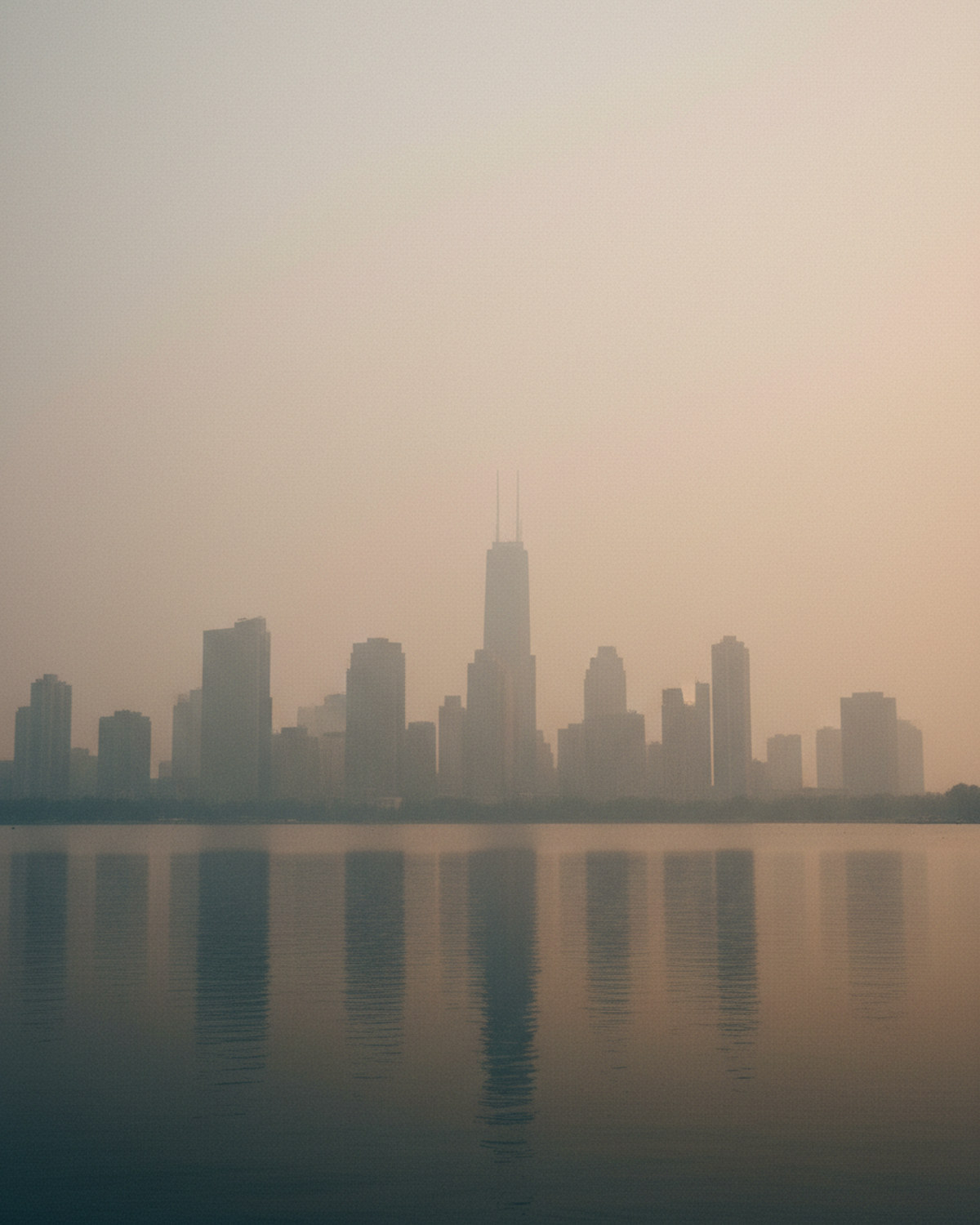 A city skyline seen faintly through a thick haze of wildfire smoke over a lakefront, with warm diffused light