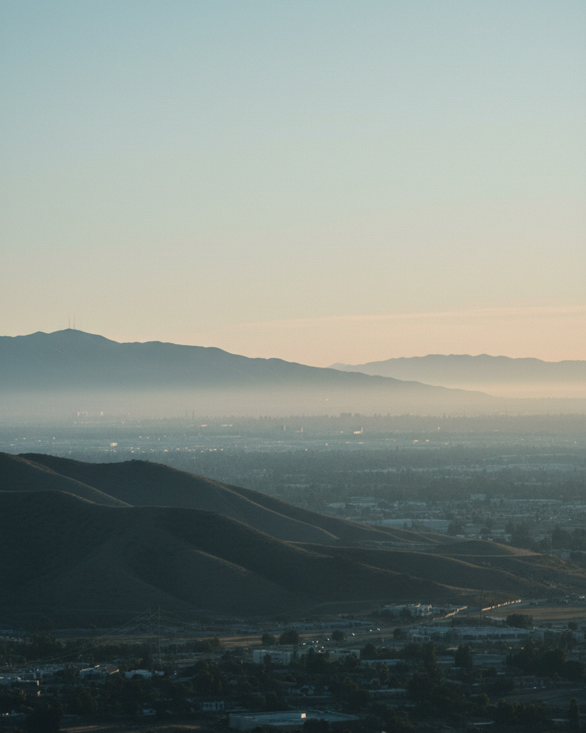 A hazy Southern California valley skyline at golden hour with heat shimmer and a thin smog haze layering the horizon